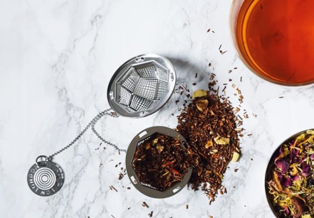Rooibos tea leaves and a tea infuser on a white marble background