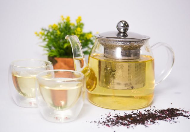 A Tea pot infuser with tea inside and 2 small glasses with tea inside