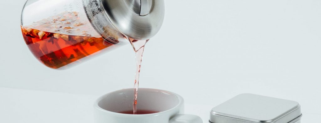 A glass tea pot pouring tea into a cup