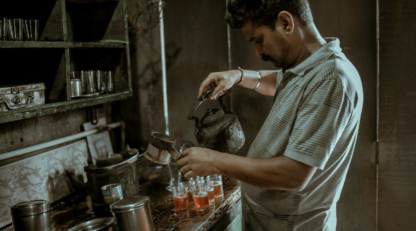 Indian man pouring several teas into glass cups.