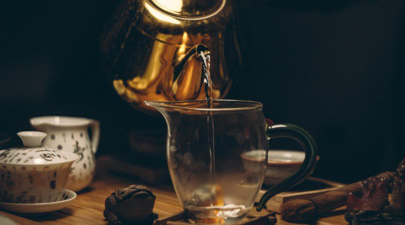 golden tea pot pouring tea into glass cup.