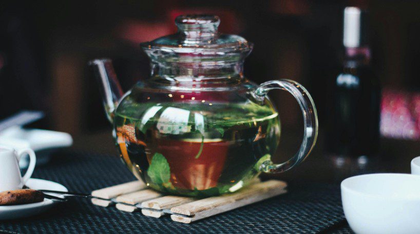 photo of a clear glass teapot with black tea and mint leaves.