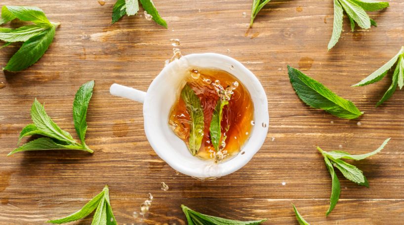Cup of peppermint tea with fresh mint leaves on a wooden surface