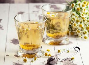 Two cups of chamomile tea with dried chamomile flowers on a white surface
