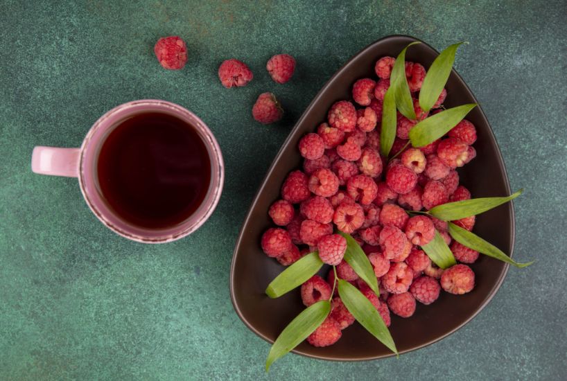 A cup of herbal tea with raspberries and fresh mint leaves on a green surface