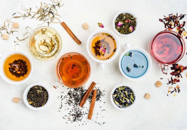 Assorted herbal teas in glass and ceramic cups with various loose leaf blends and ingredients on a white background