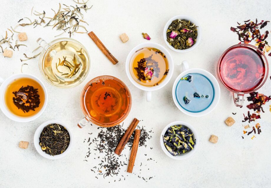 Assorted herbal teas in glass and ceramic cups with various loose leaf blends and ingredients on a white background