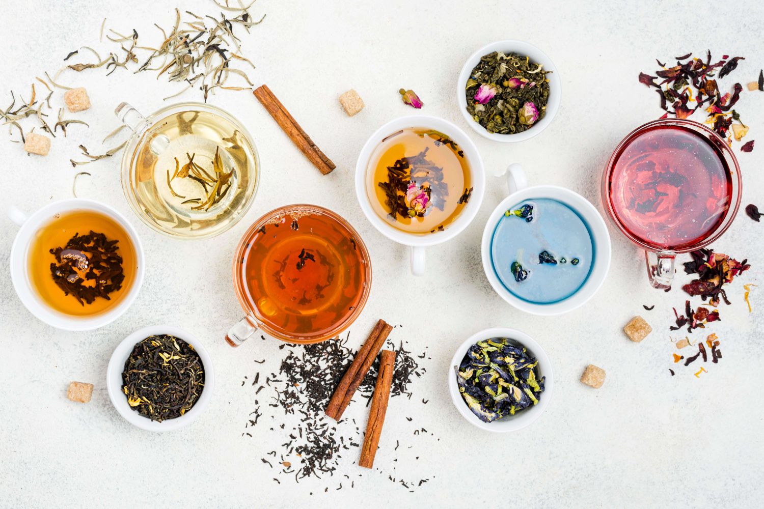 Assorted herbal teas in glass and ceramic cups with various loose leaf blends and ingredients on a white background