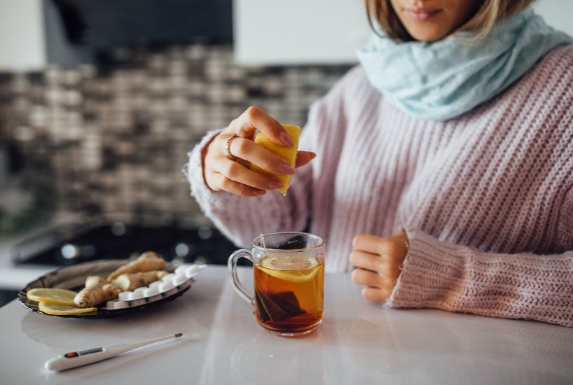 Person enjoying a warm cup of Pu-erh tea with lemon and ginger, highlighting its soothing and health-boosting properties.