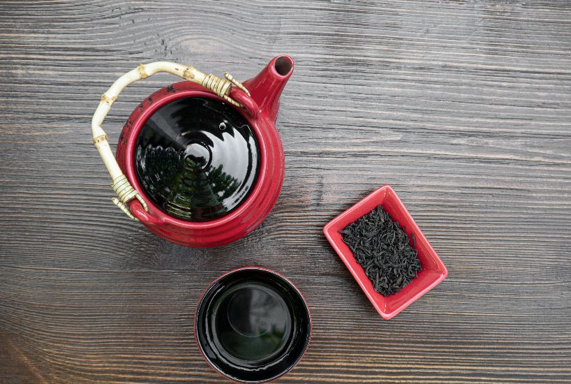 Freshly brewed Pu-erh tea served in a traditional red teapot with loose tea leaves on a wooden table.